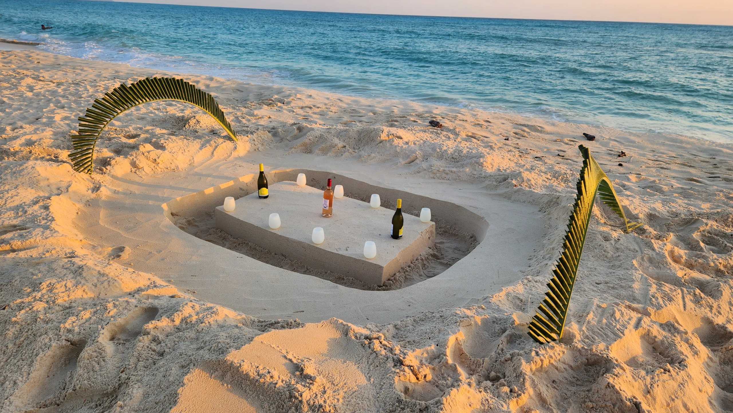 A table carved into the sand at sunset, set with candles and lit by the last of the light