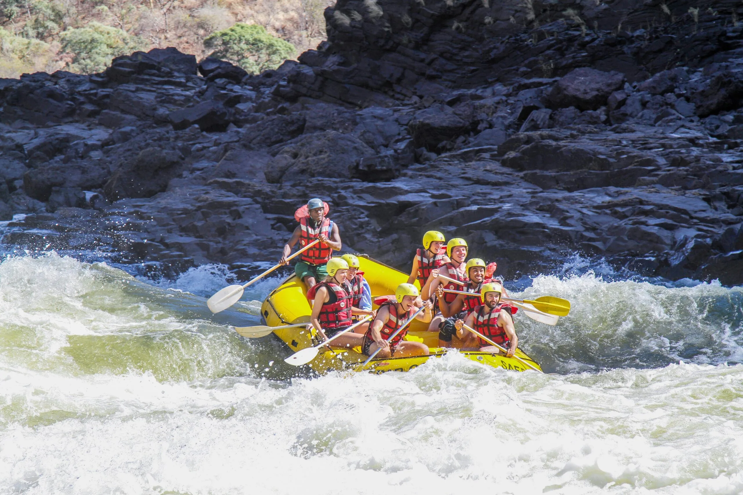 A raft crew paddling hard through white water below a rock gorge