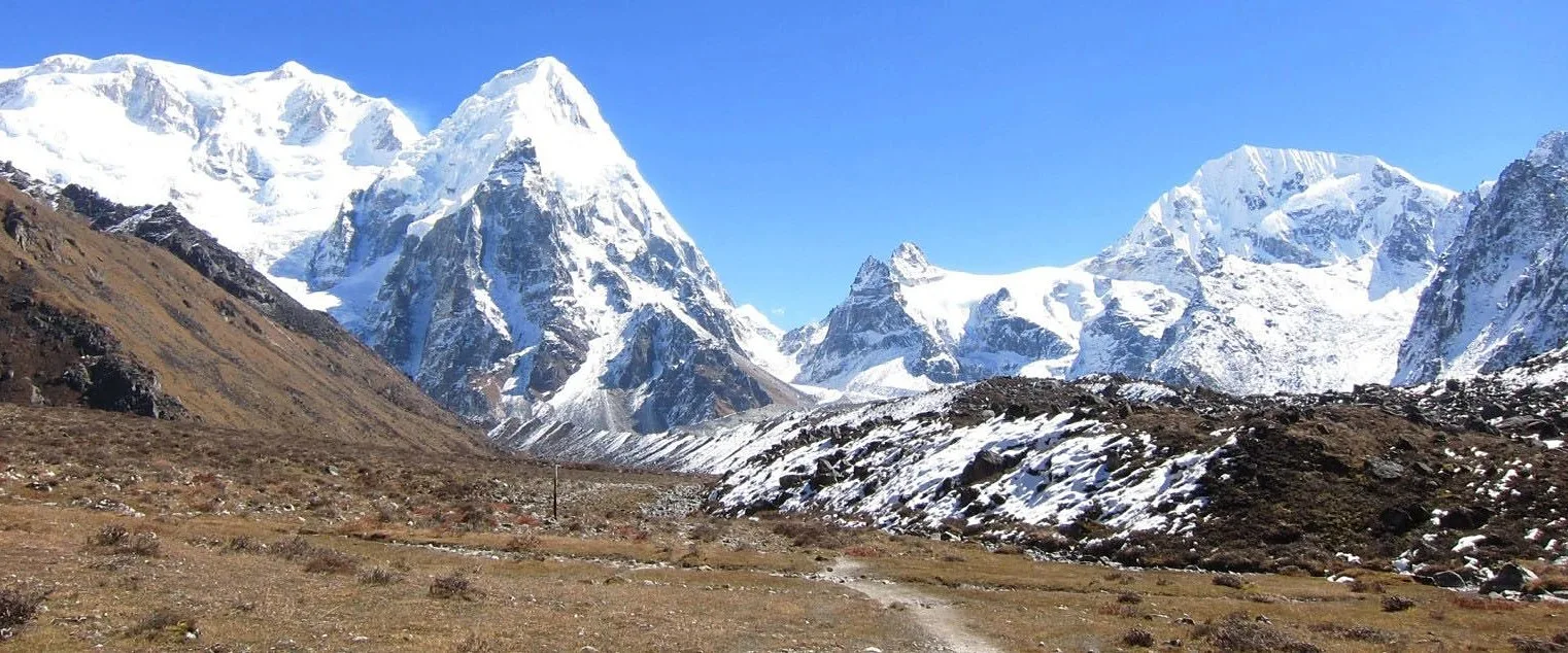 A path across a valley floor towards snow-covered Himalayan peaks