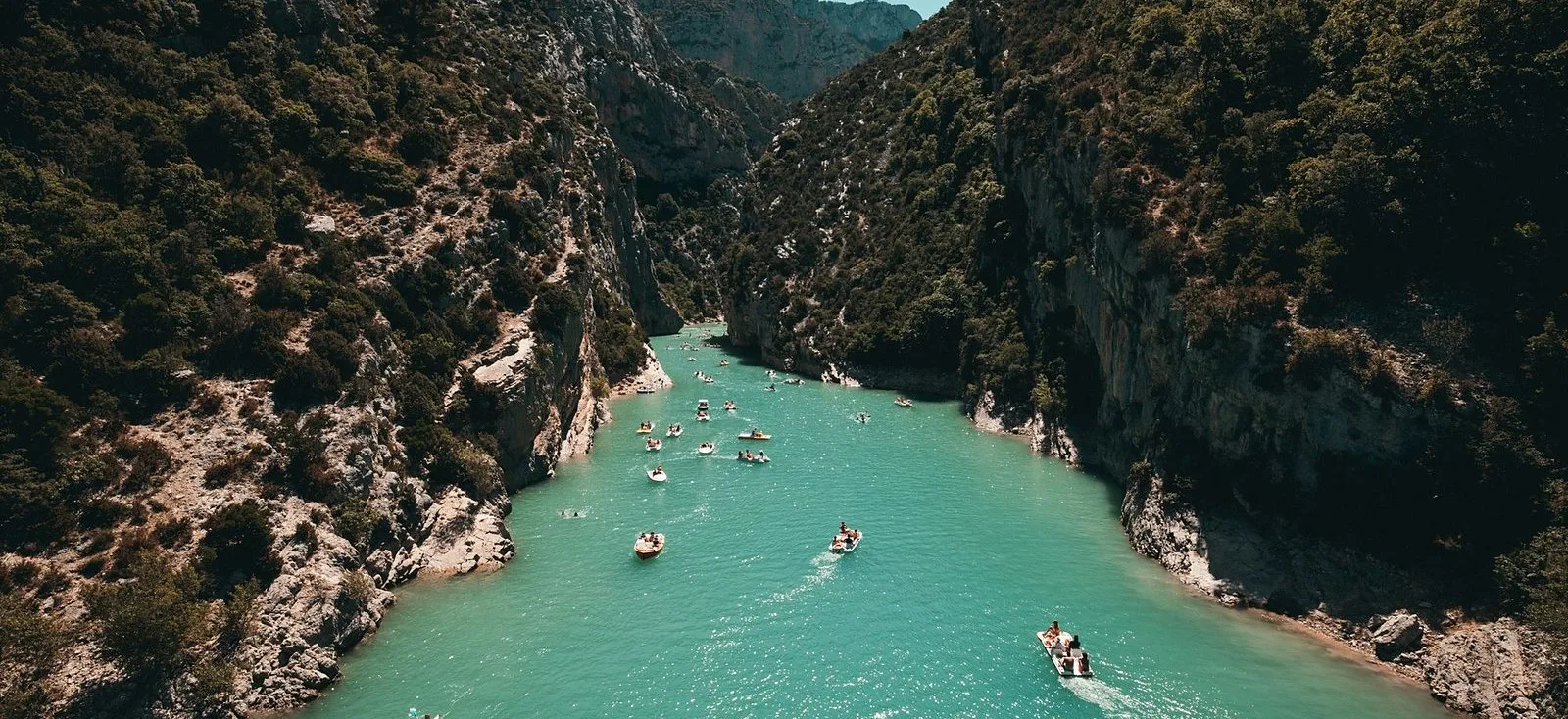 Small boats strung out along a turquoise river between limestone cliffs, seen from above